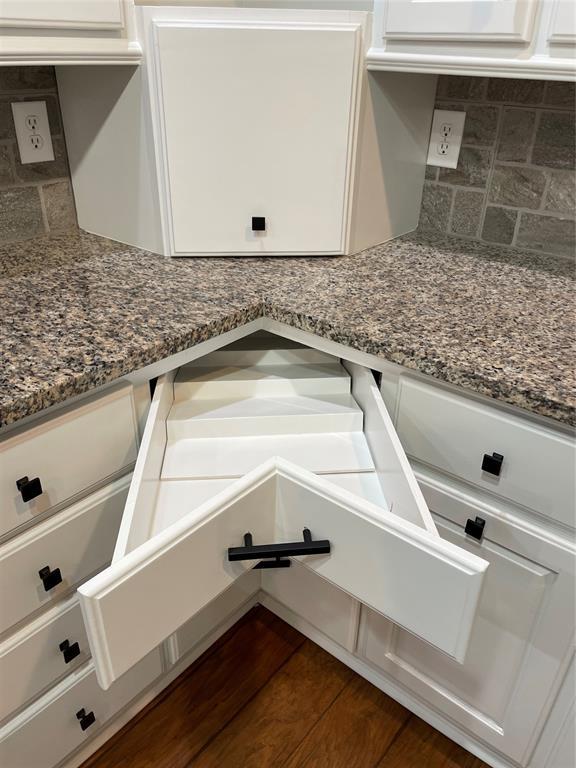 interior details with dark wood-type flooring, dark stone counters, white cabinets, and backsplash