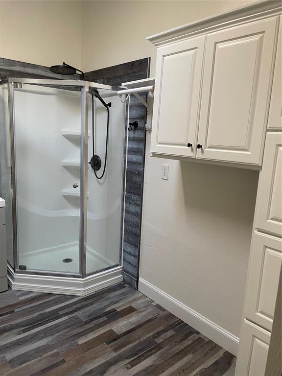 full bath with a stall shower, baseboards, and wood finished floors