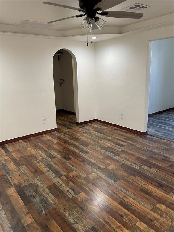 spare room with arched walkways, dark wood-style floors, visible vents, and baseboards