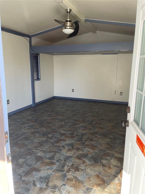 empty room with vaulted ceiling with beams, ceiling fan, baseboards, and stone finish flooring