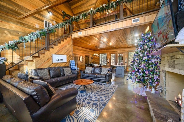 living room with wooden walls, lofted ceiling with beams, wooden ceiling, concrete floors, and a stone fireplace