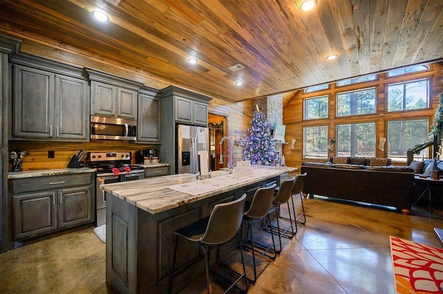 kitchen with wood walls, wooden ceiling, an island with sink, a kitchen bar, and stainless steel appliances