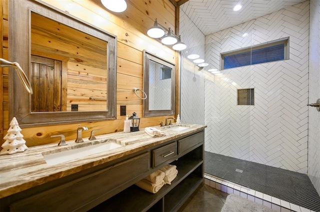 bathroom with a tile shower, wooden walls, tile patterned floors, and vanity