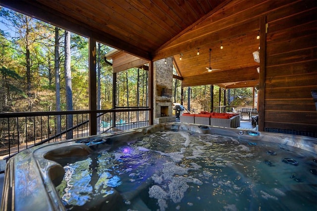 wooden terrace featuring an outdoor stone fireplace and a hot tub