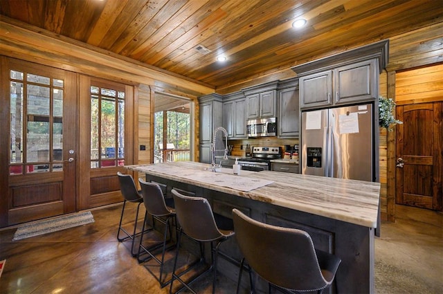 607 Sugar Pine Loop, Broken Bow, OK 74728 - kitchen featuring appliances with stainless steel finishes, concrete flooring, wood ceiling, wood walls, and a kitchen breakfast bar