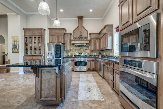 kitchen featuring pendant lighting, custom exhaust hood, a center island, dark stone countertops, and appliances with stainless steel finishes