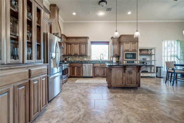 kitchen with pendant lighting, backsplash, crown molding, a kitchen island, and stainless steel appliances