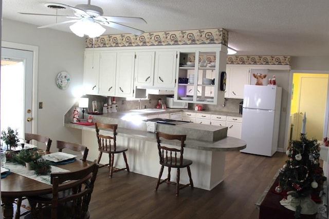 kitchen with kitchen peninsula, white appliances, white cabinets, and a breakfast bar area