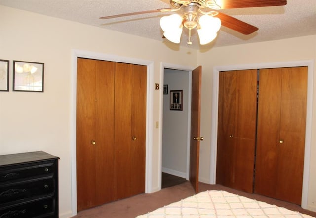 unfurnished bedroom with two closets, a textured ceiling, carpet floors, and ceiling fan