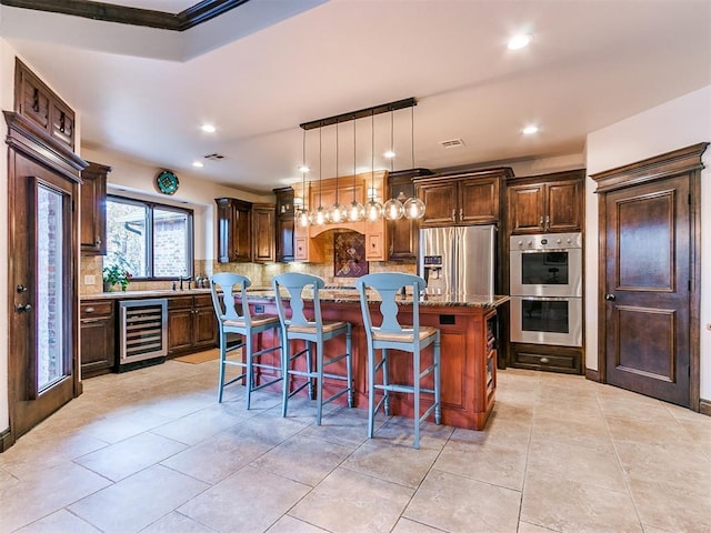 kitchen with stone counters, a kitchen breakfast bar, stainless steel appliances, a kitchen island, and beverage cooler