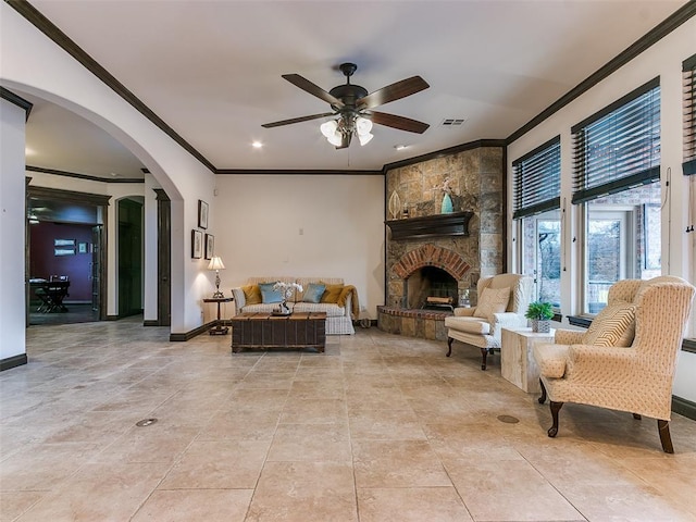 tiled living room with ornamental molding, a stone fireplace, and ceiling fan