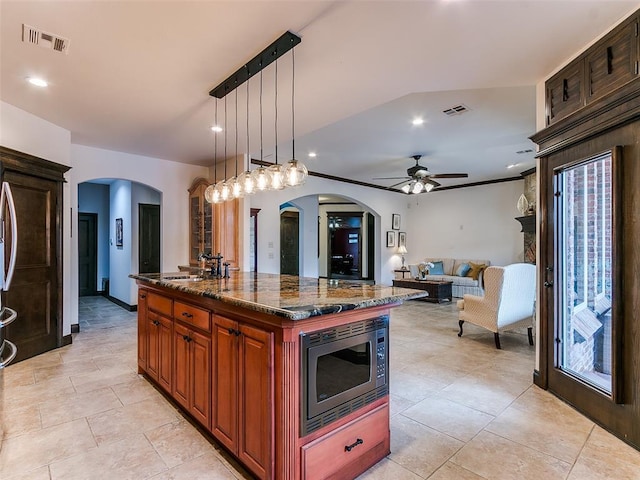 kitchen with pendant lighting, sink, a center island, stainless steel microwave, and dark stone counters