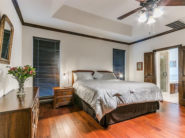 bedroom with crown molding, hardwood / wood-style floors, a tray ceiling, and connected bathroom