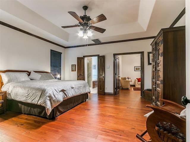 bedroom with ensuite bathroom, hardwood / wood-style floors, ceiling fan, a tray ceiling, and crown molding