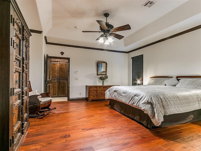 bedroom with ceiling fan, ornamental molding, wood-type flooring, and a tray ceiling