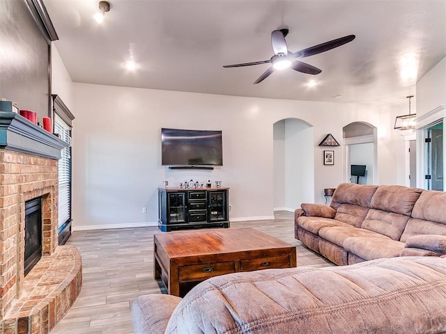 living room with ceiling fan, wood-type flooring, and a brick fireplace