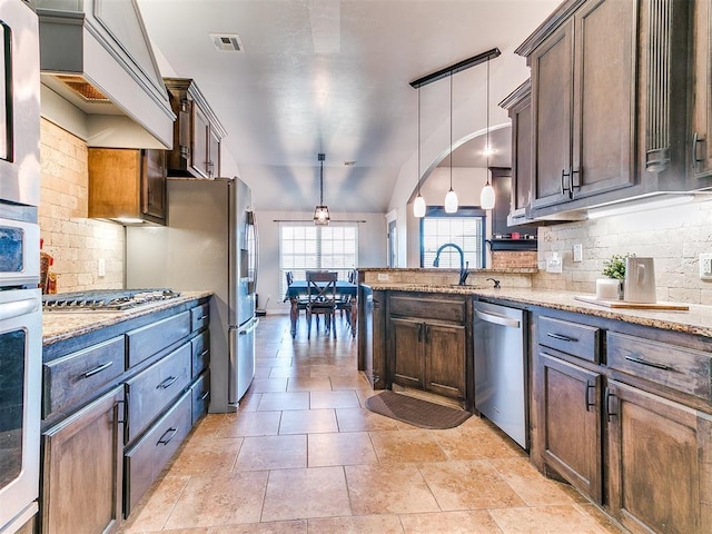 kitchen with decorative backsplash, appliances with stainless steel finishes, light stone counters, dark brown cabinets, and pendant lighting