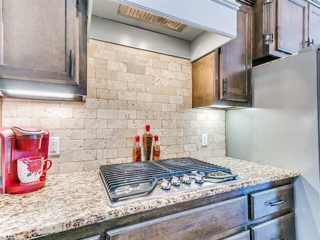 kitchen featuring stainless steel appliances, dark brown cabinetry, backsplash, and exhaust hood