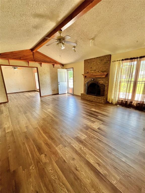 15268 Pheasant Run, Choctaw, OK 73020 - unfurnished living room with a textured ceiling, ceiling fan, wood finished floors, a brick fireplace, and baseboards
