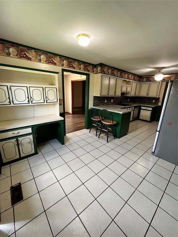 15268 Pheasant Run, Choctaw, OK 73020 - kitchen with light tile patterned floors, a peninsula, freestanding refrigerator, and a kitchen bar