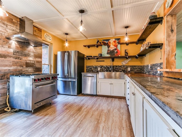 kitchen featuring white cabinets, wall chimney range hood, sink, appliances with stainless steel finishes, and decorative light fixtures