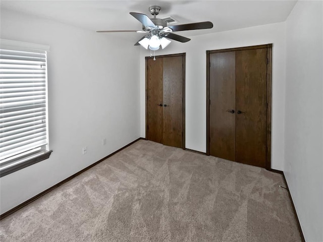 unfurnished bedroom with multiple closets, ceiling fan, and light carpet