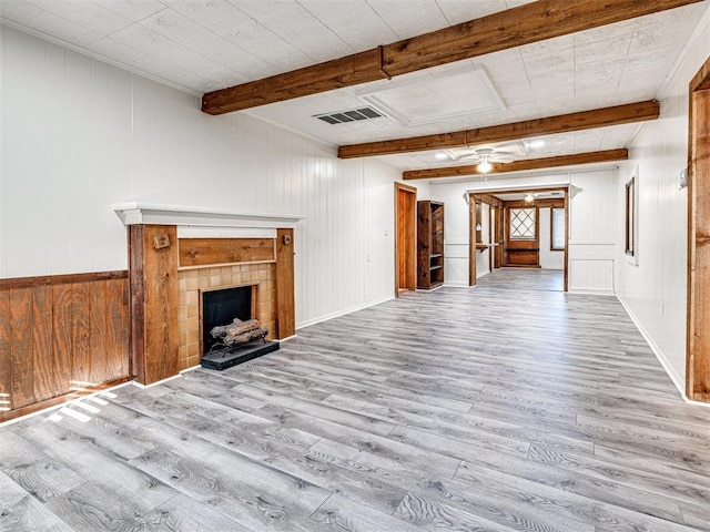 unfurnished living room with beamed ceiling, light wood-type flooring, wooden walls, and a tiled fireplace