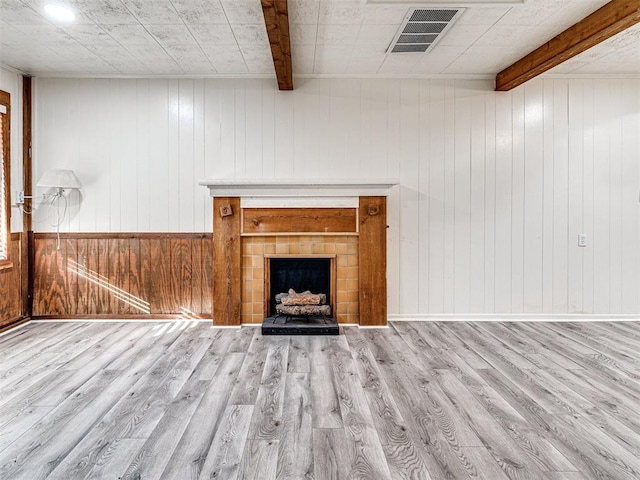 unfurnished living room featuring wood walls, light hardwood / wood-style floors, and beamed ceiling