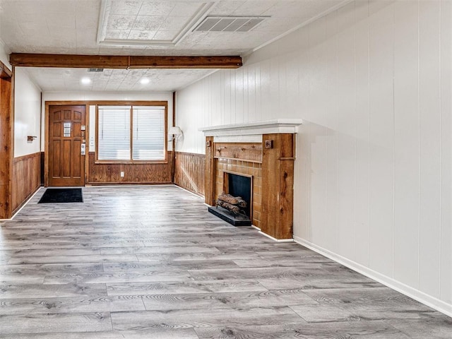 unfurnished living room with beamed ceiling, light wood-type flooring, a tile fireplace, and wooden walls