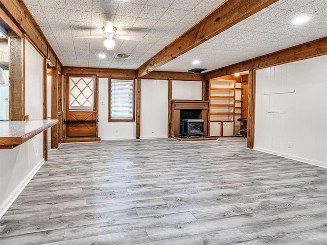 unfurnished living room with a wood stove, ceiling fan, light hardwood / wood-style flooring, and beamed ceiling