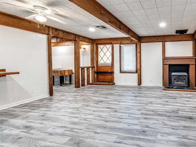 unfurnished living room featuring beamed ceiling, light hardwood / wood-style floors, ceiling fan, and wood walls