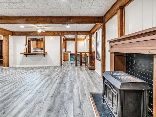 miscellaneous room featuring light wood-type flooring, ceiling fan, wooden walls, beam ceiling, and a wood stove