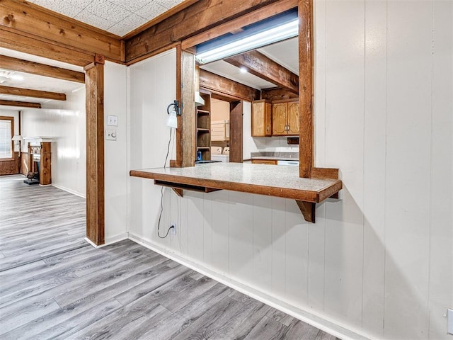 kitchen featuring beam ceiling, kitchen peninsula, wooden walls, and light hardwood / wood-style flooring