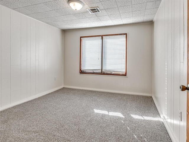 carpeted empty room featuring a drop ceiling and wood walls