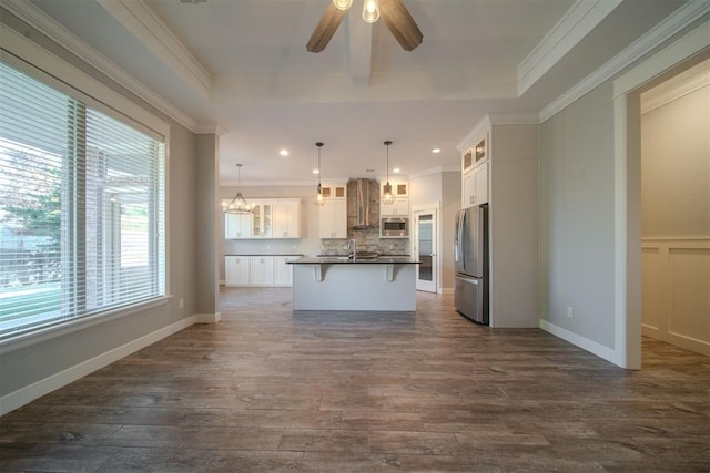 kitchen with decorative light fixtures, stainless steel appliances, white cabinetry, and a kitchen island with sink