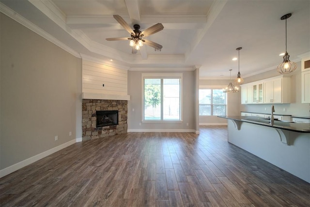 unfurnished living room with dark hardwood / wood-style flooring, ornamental molding, ceiling fan, sink, and a stone fireplace