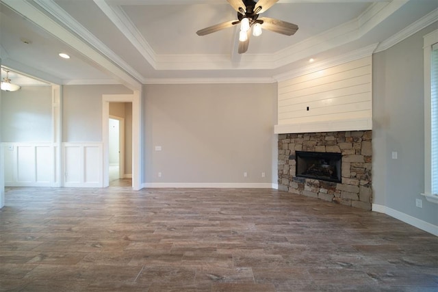 unfurnished living room featuring ceiling fan, a raised ceiling, a stone fireplace, wood-type flooring, and ornamental molding