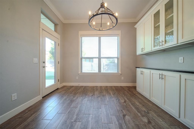 unfurnished dining area with crown molding, dark wood-type flooring, and an inviting chandelier