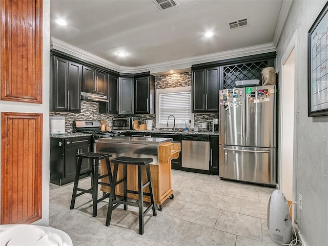 kitchen with a center island, stainless steel appliances, decorative backsplash, a breakfast bar, and ornamental molding