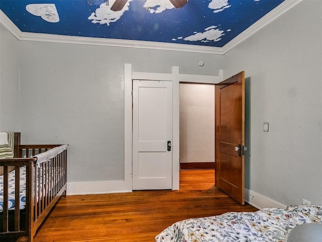 bedroom with hardwood / wood-style floors, a nursery area, ceiling fan, and ornamental molding