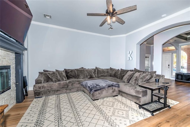 living room with hardwood / wood-style floors, a stone fireplace, ceiling fan, and crown molding