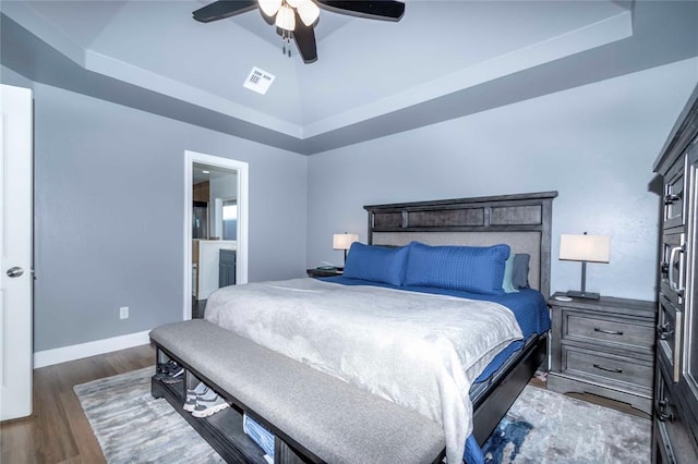 bedroom with dark hardwood / wood-style floors, ceiling fan, a raised ceiling, and ensuite bath