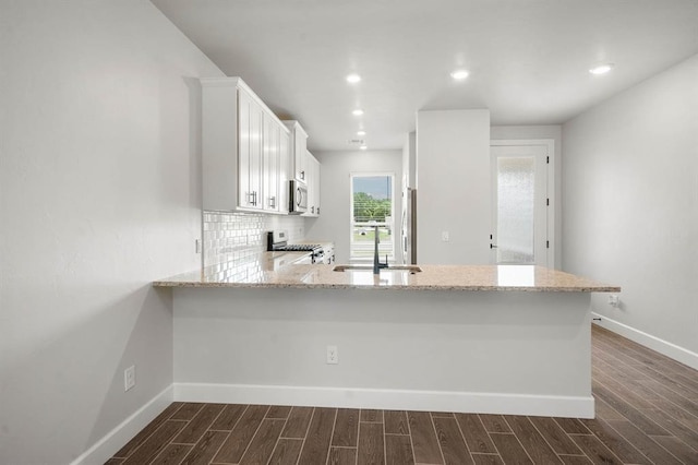 kitchen featuring kitchen peninsula, appliances with stainless steel finishes, dark hardwood / wood-style flooring, sink, and white cabinetry