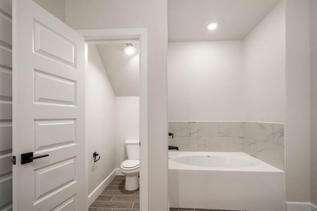 bathroom featuring hardwood / wood-style floors, vaulted ceiling, toilet, and a tub