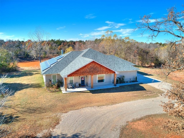 view of front of property featuring solar panels, a front yard, driveway, roof with shingles, and a patio area