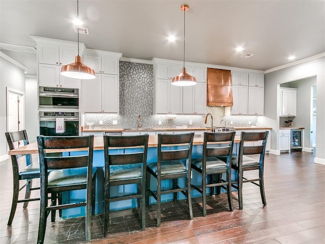 kitchen with pendant lighting, a kitchen island with sink, custom exhaust hood, and white cabinetry