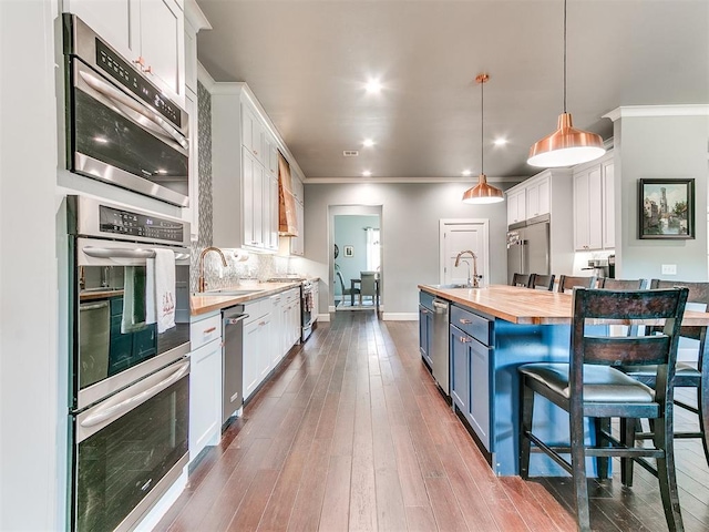 kitchen with white cabinets, butcher block countertops, decorative light fixtures, blue cabinets, and a kitchen bar