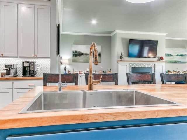 kitchen with tasteful backsplash, white cabinets, wood counters, ornamental molding, and a fireplace