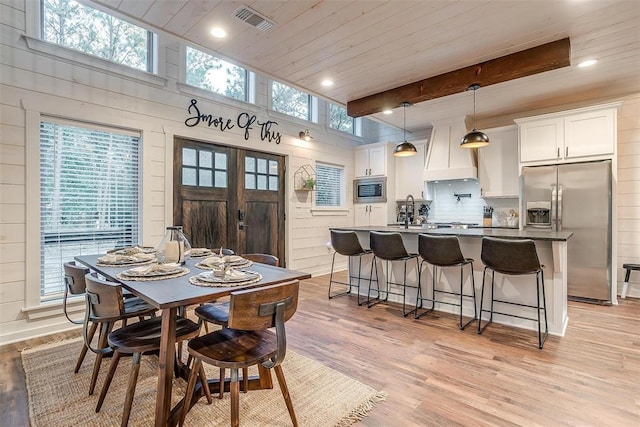 dining area with plenty of natural light, light wood-type flooring, wooden walls, and french doors