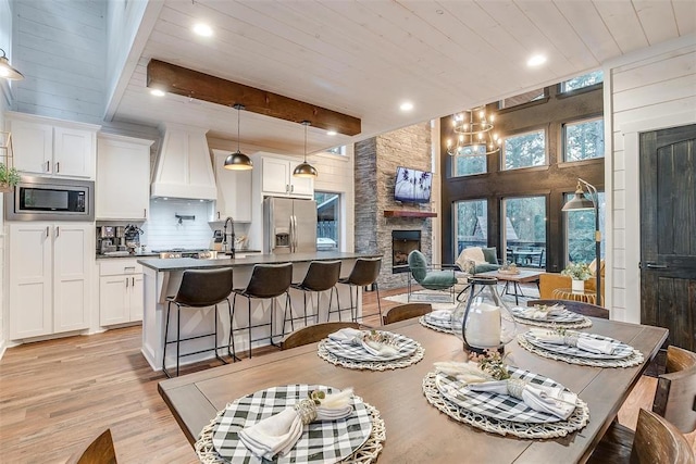 dining area featuring a stone fireplace, sink, light hardwood / wood-style floors, beam ceiling, and a chandelier